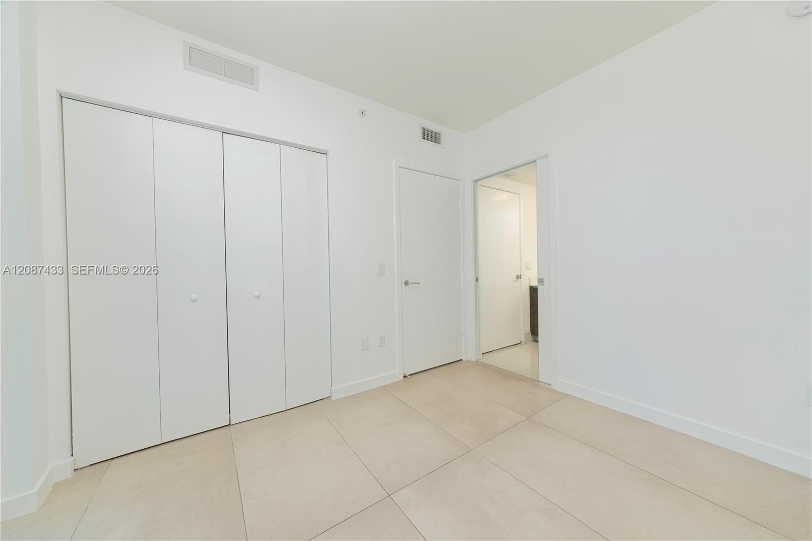 Empty tiled room with a wide built-in closet and doorway to an adjoining bathroom.