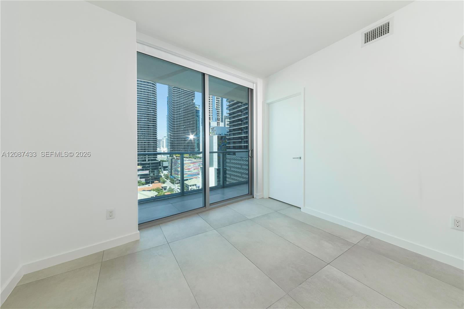 Vacant tiled room with sliding glass doors opening to a balcony and city views.