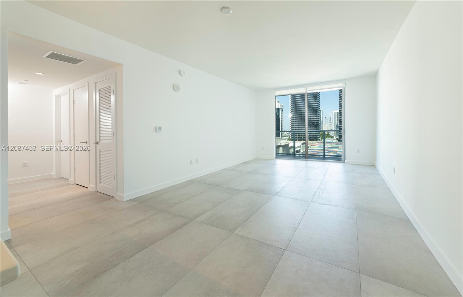 Vacant condo living room with large tile floors and balcony doors overlooking downtown high-rises.