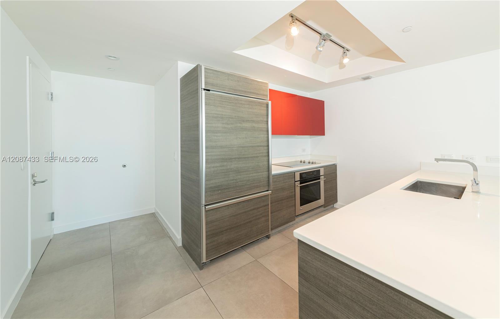 Modern condo kitchen with a white island, gray cabinetry, and bright red upper cabinets.