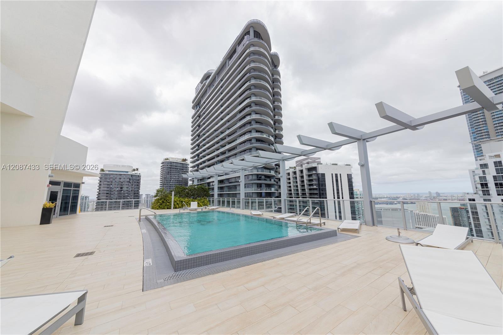 Rooftop pool deck with white loungers, a pergola, and views of surrounding Miami high-rises.