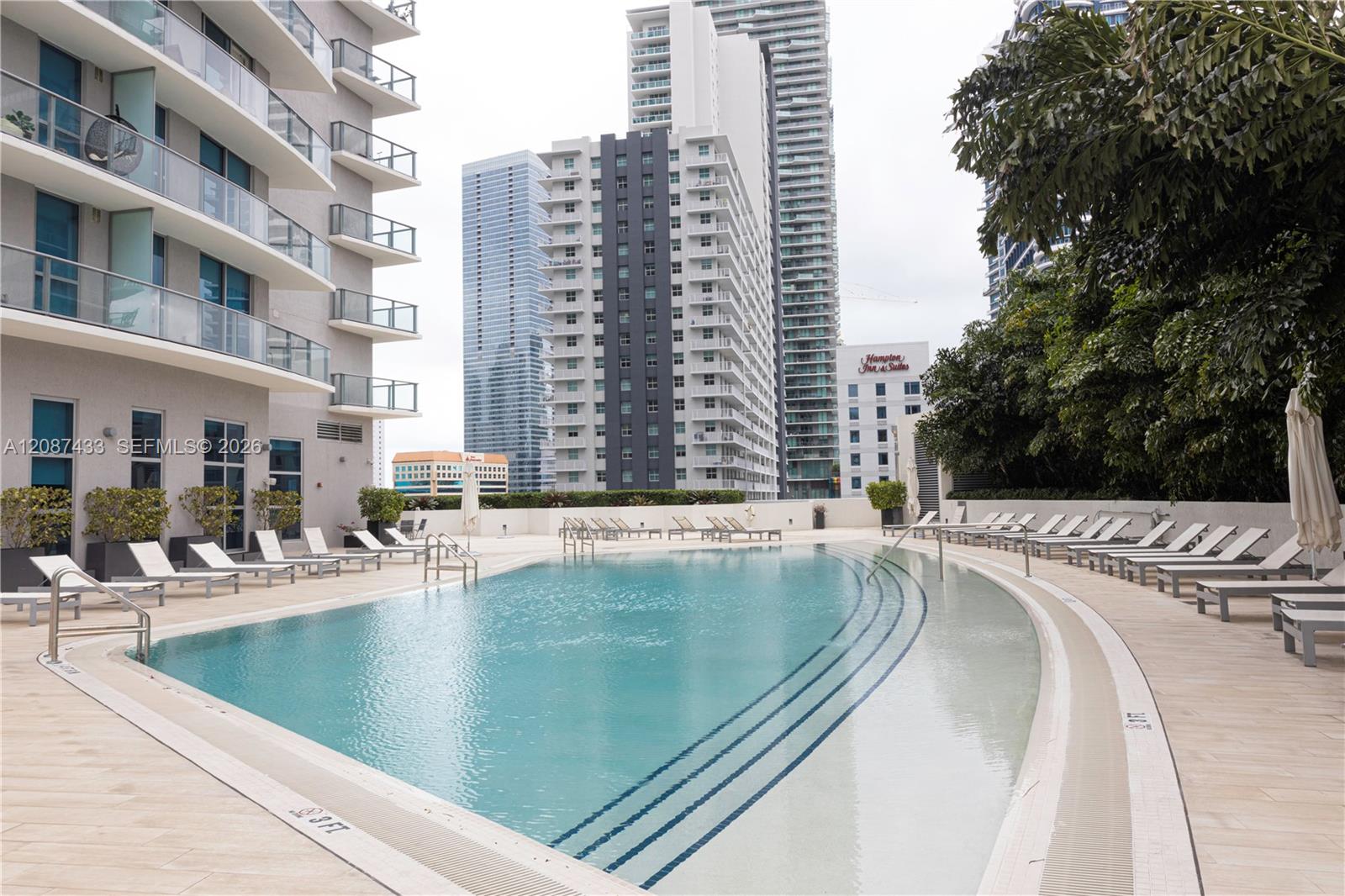 Condominium pool with curved swimming lanes, sun loungers, and high-rise buildings in the background.