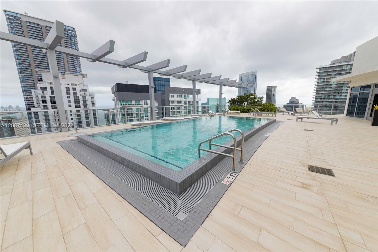 Rooftop condominium pool with tiled deck, pergola, lounge chairs, and surrounding Miami high-rises.