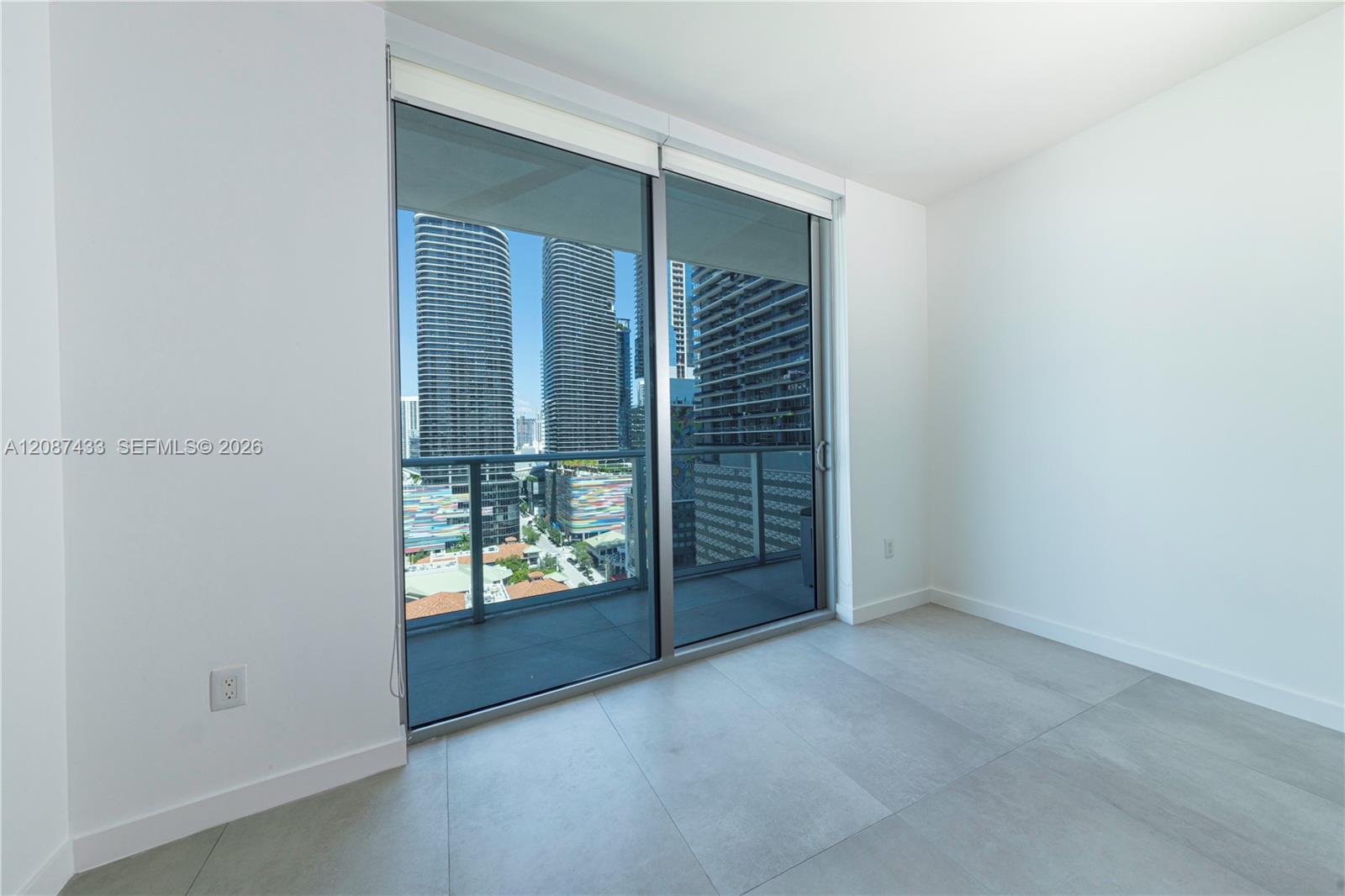 Empty condo room with sliding glass doors opening to a balcony and a view of downtown high-rises.