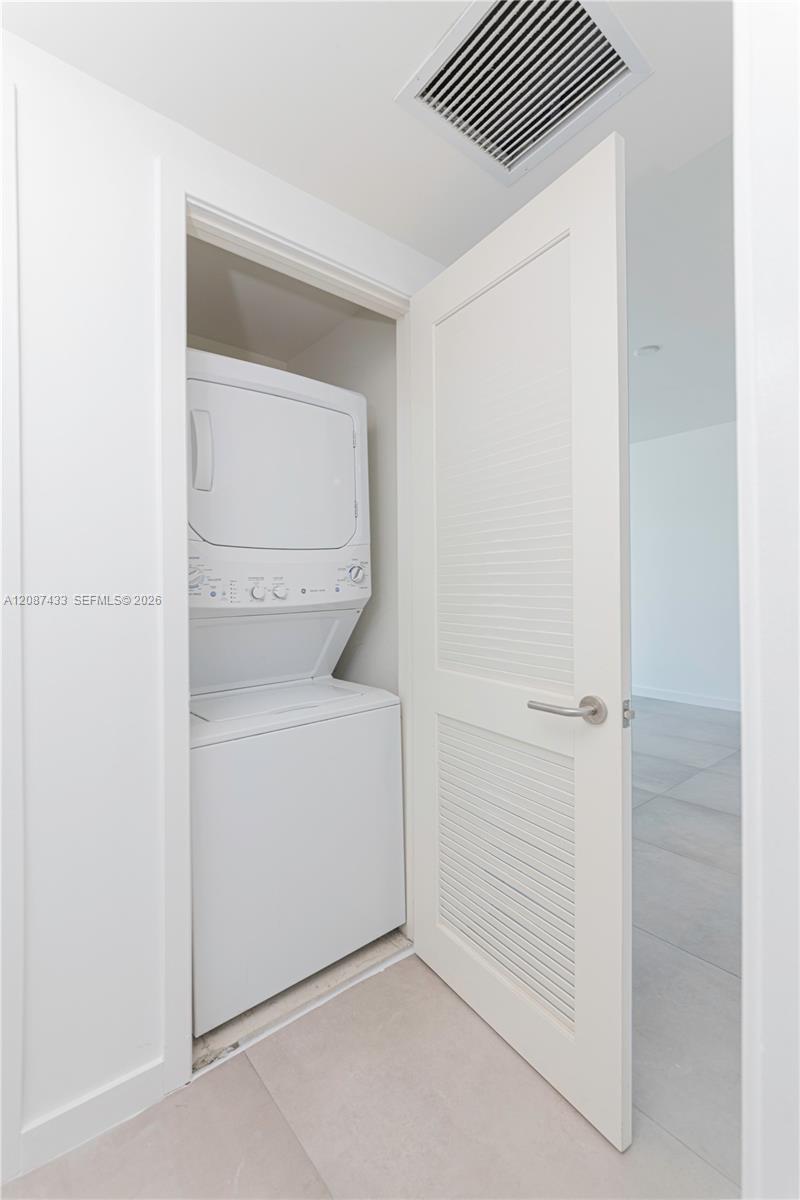 Laundry closet with a stacked washer and dryer behind an open louvered door.
