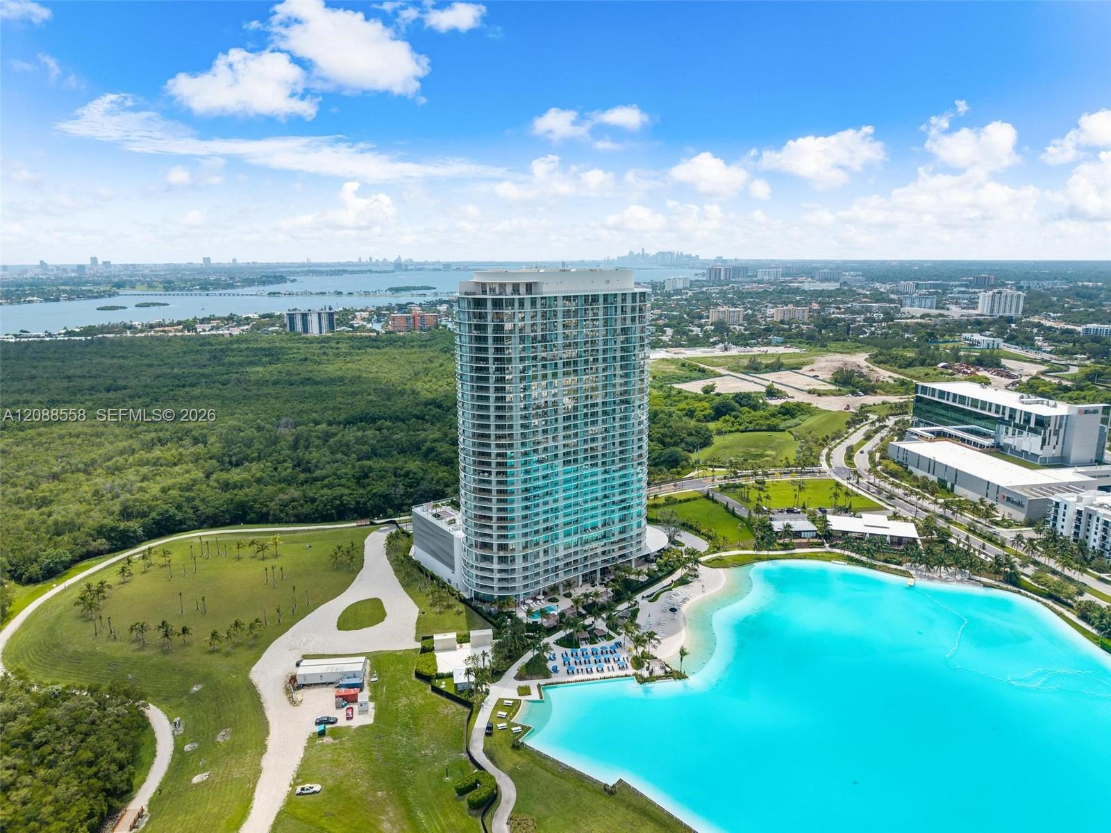 Curved condominium tower beside a turquoise pool, with bay and distant city views.