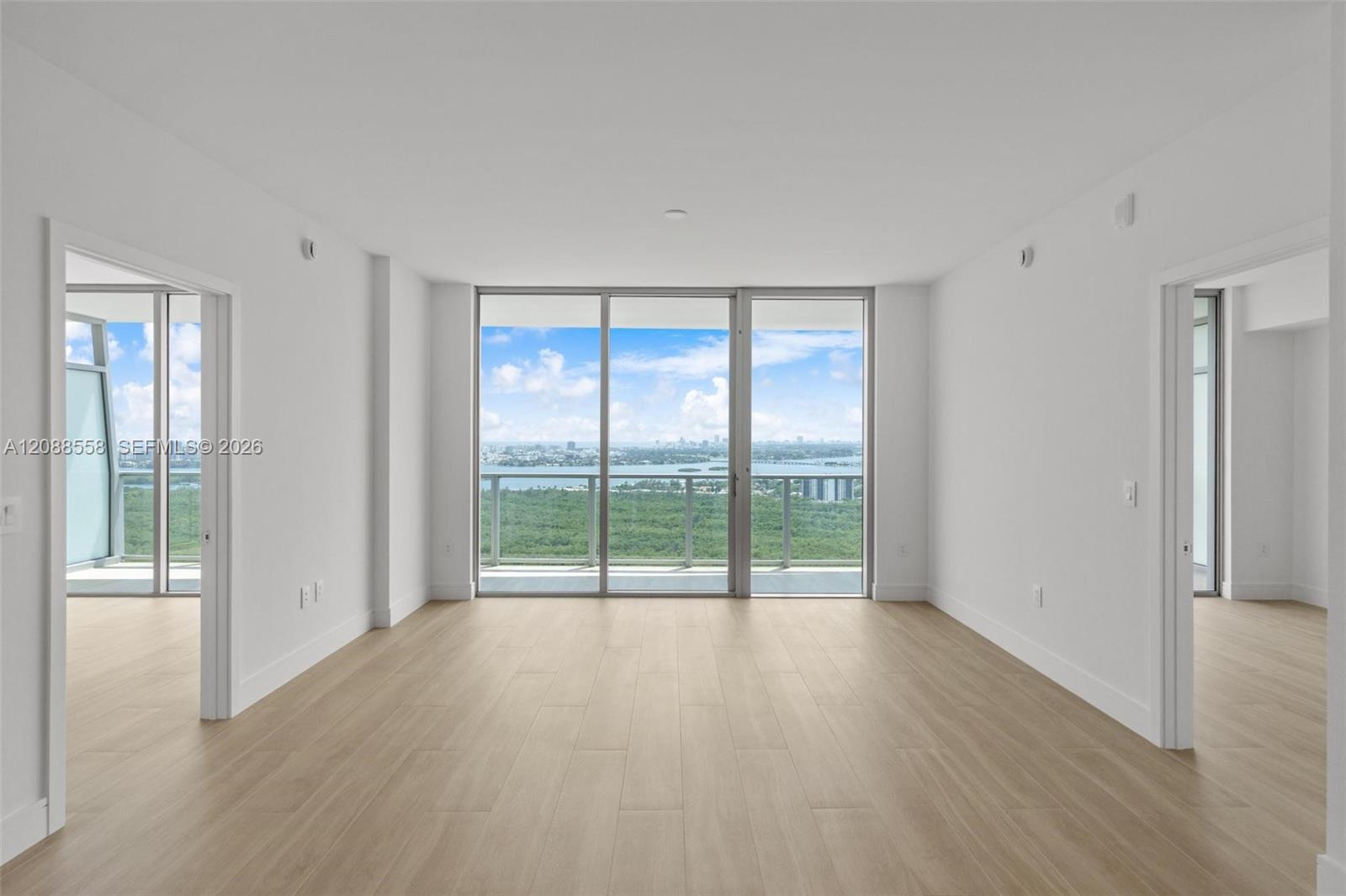 Empty room with pale wood floors and floor-to-ceiling windows overlooking water and greenery.