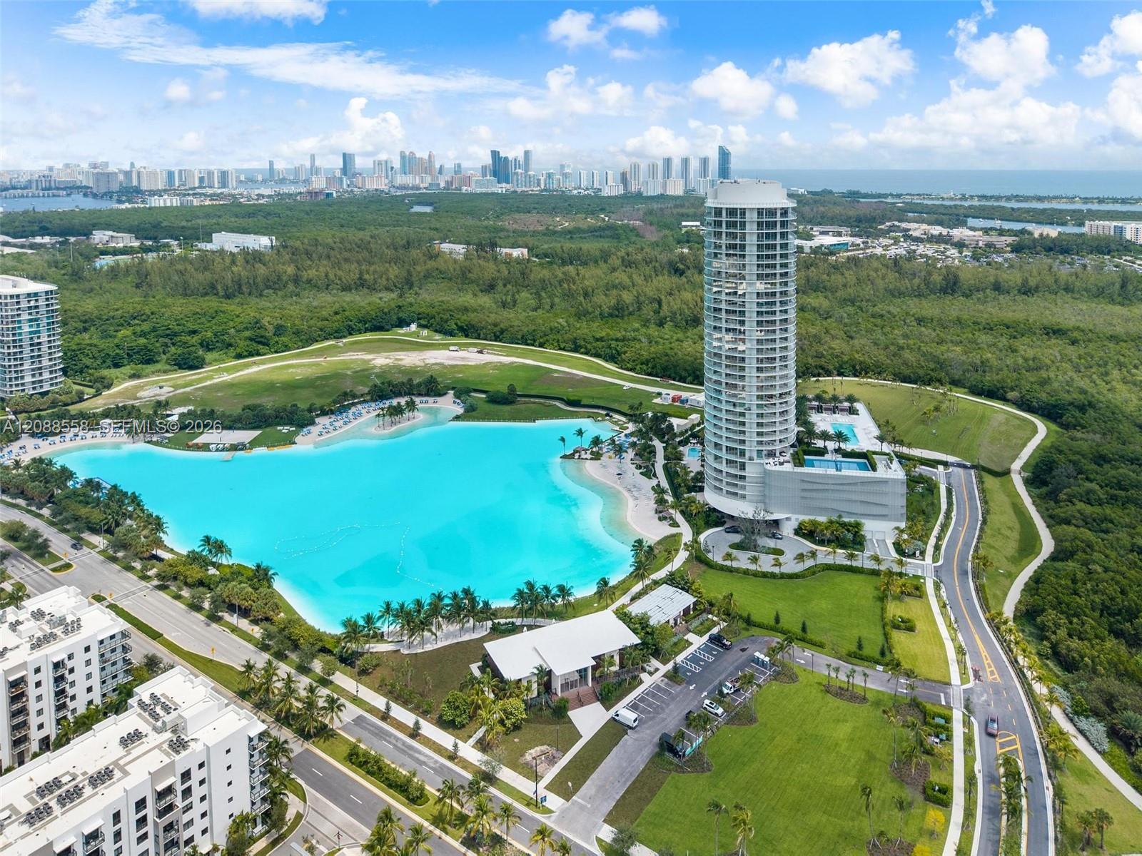 Aerial view of a high-rise beside a turquoise lagoon, with Miami’s skyline and ocean beyond.