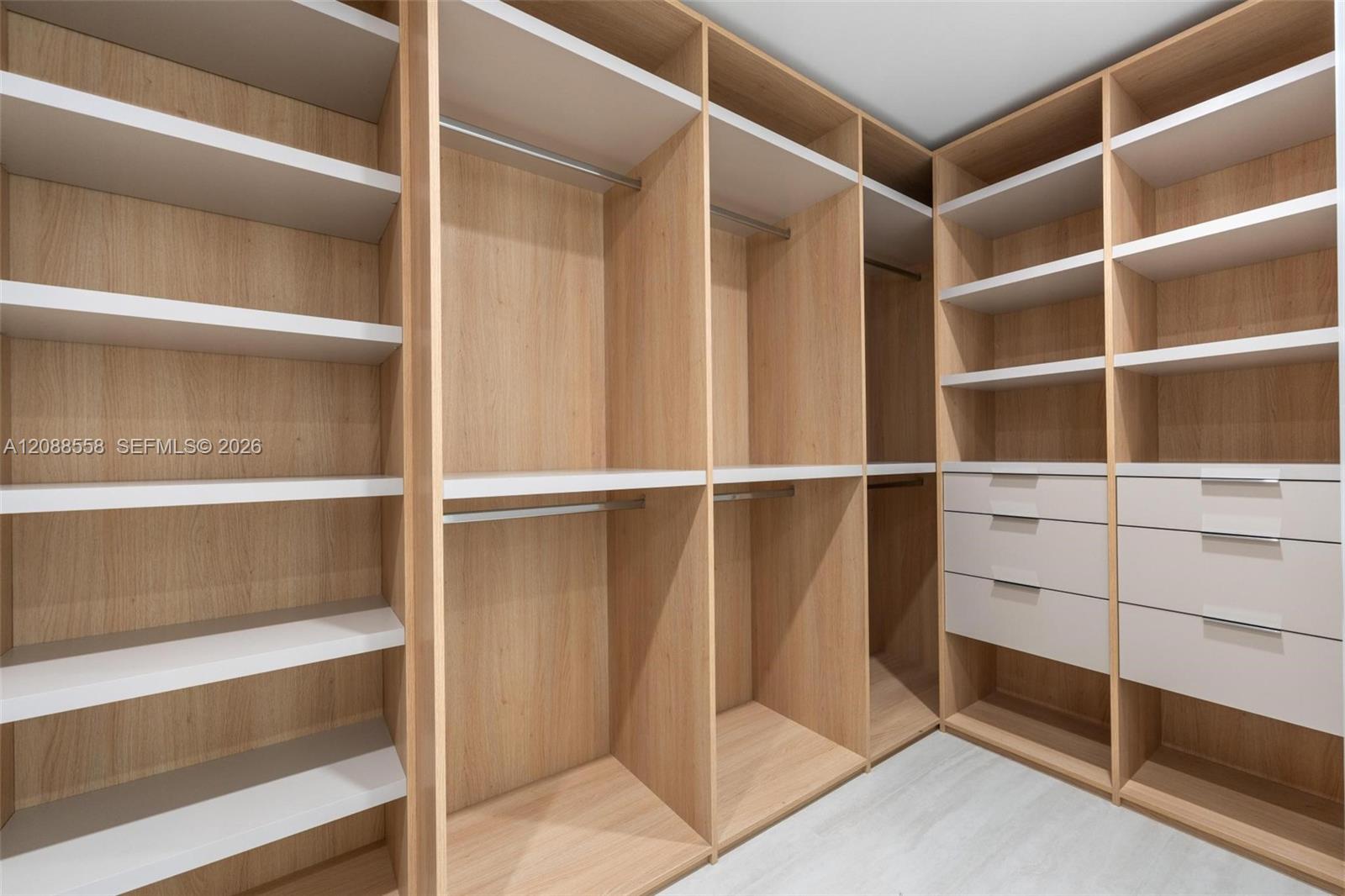 Walk-in closet with light wood shelving, hanging rods, and built-in white drawers.