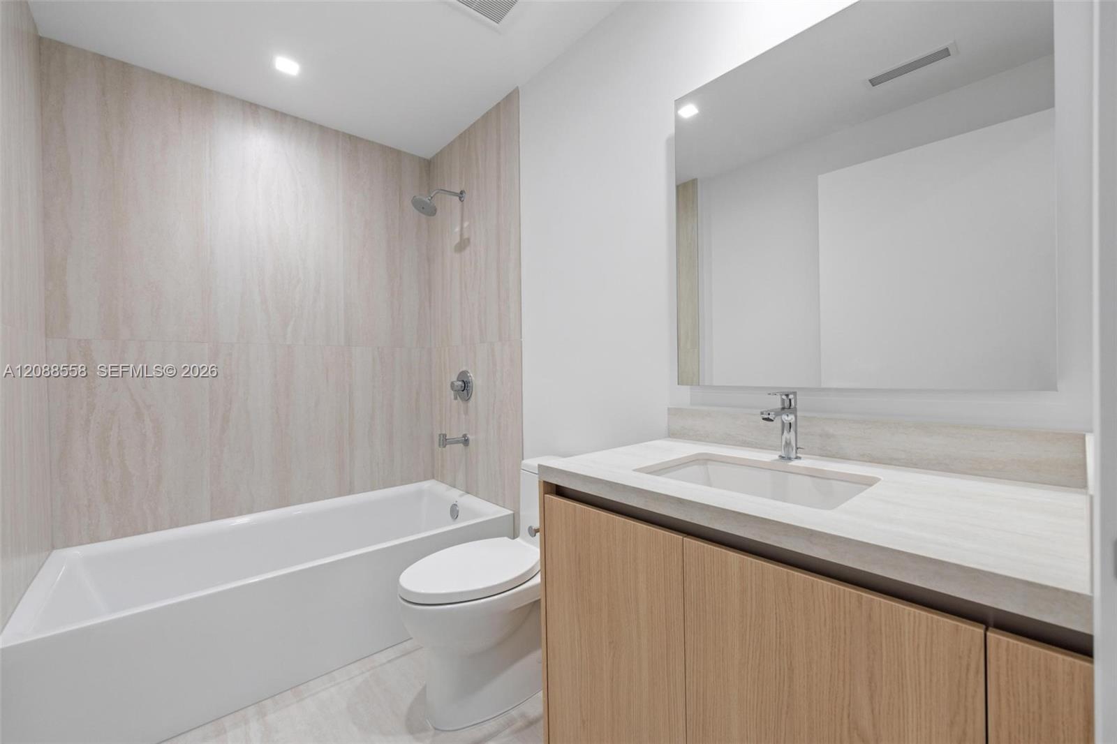 Modern bathroom with a tiled tub and shower beside a wood-front vanity.