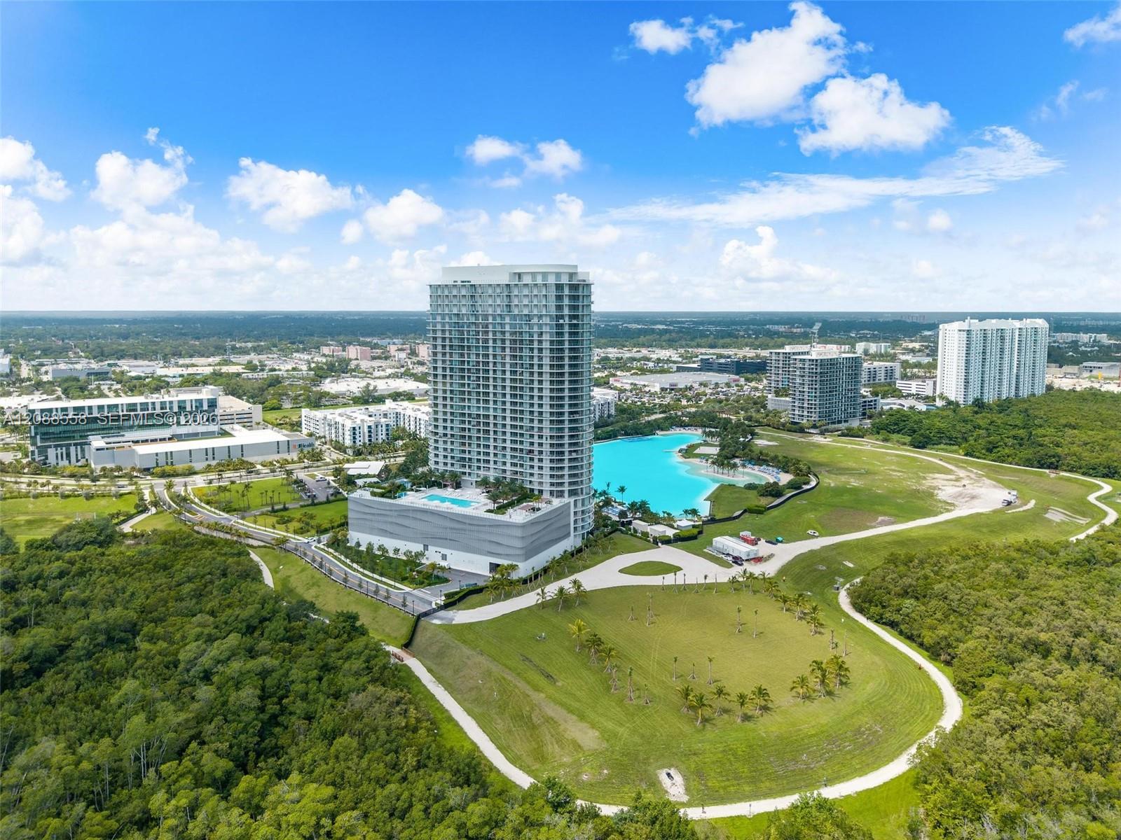 Aerial view of a modern condominium tower beside a turquoise lagoon pool and landscaped grounds.