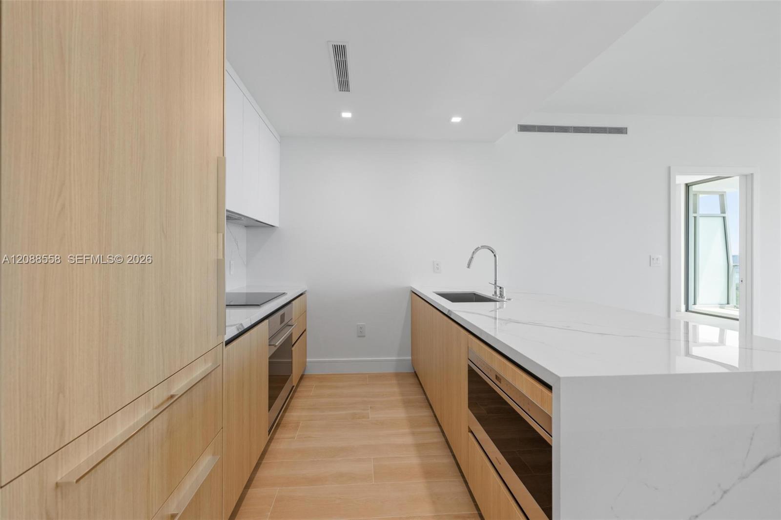 Modern kitchen with light wood cabinets, a white stone island, and built-in appliances.