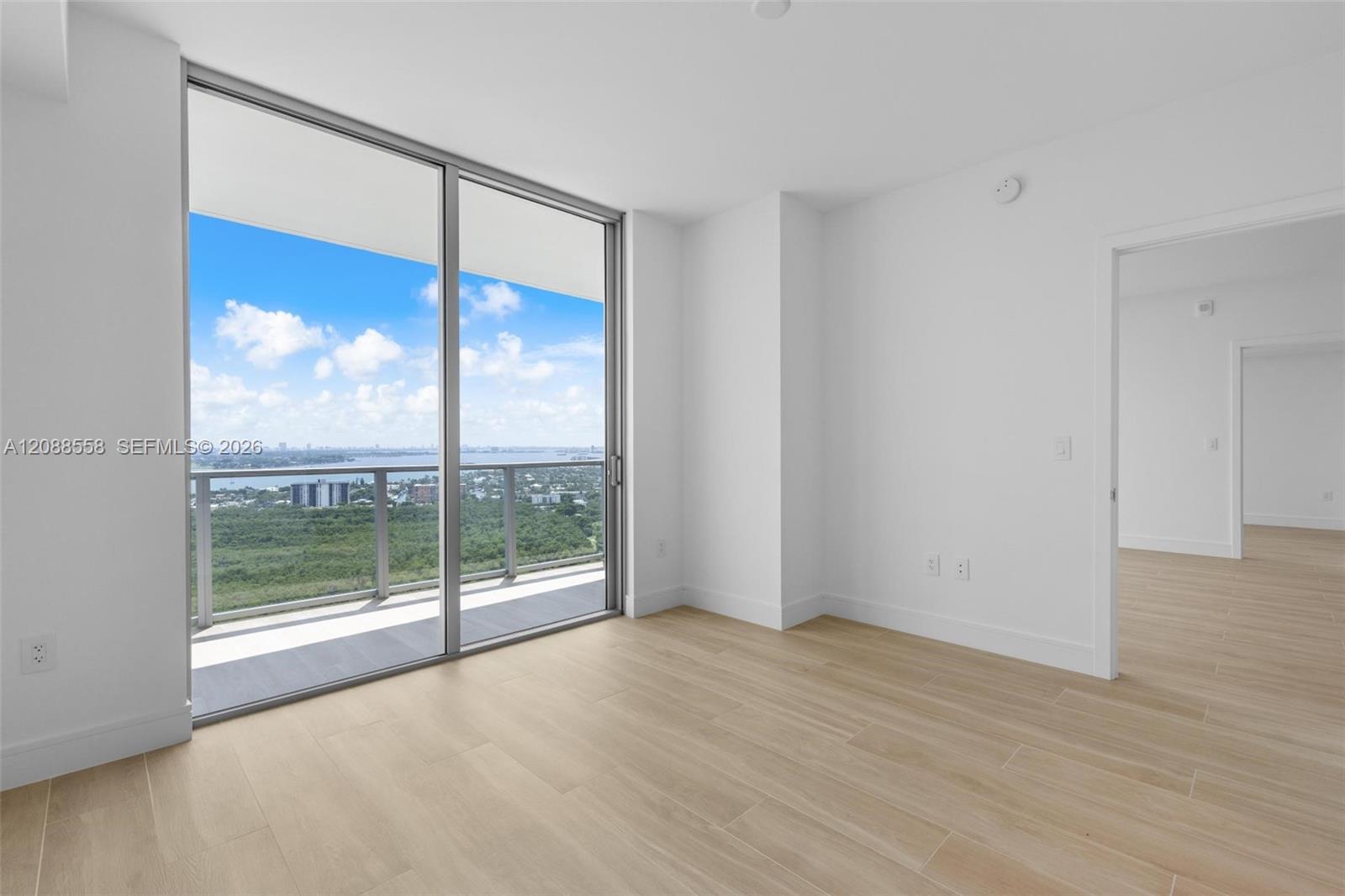 Empty modern room with wood-look tile and sliding doors opening to a balcony overlooking water.