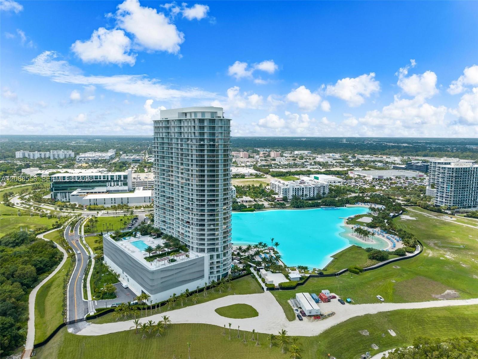 Aerial view of a curved residential tower beside a turquoise lagoon pool and landscaped grounds.