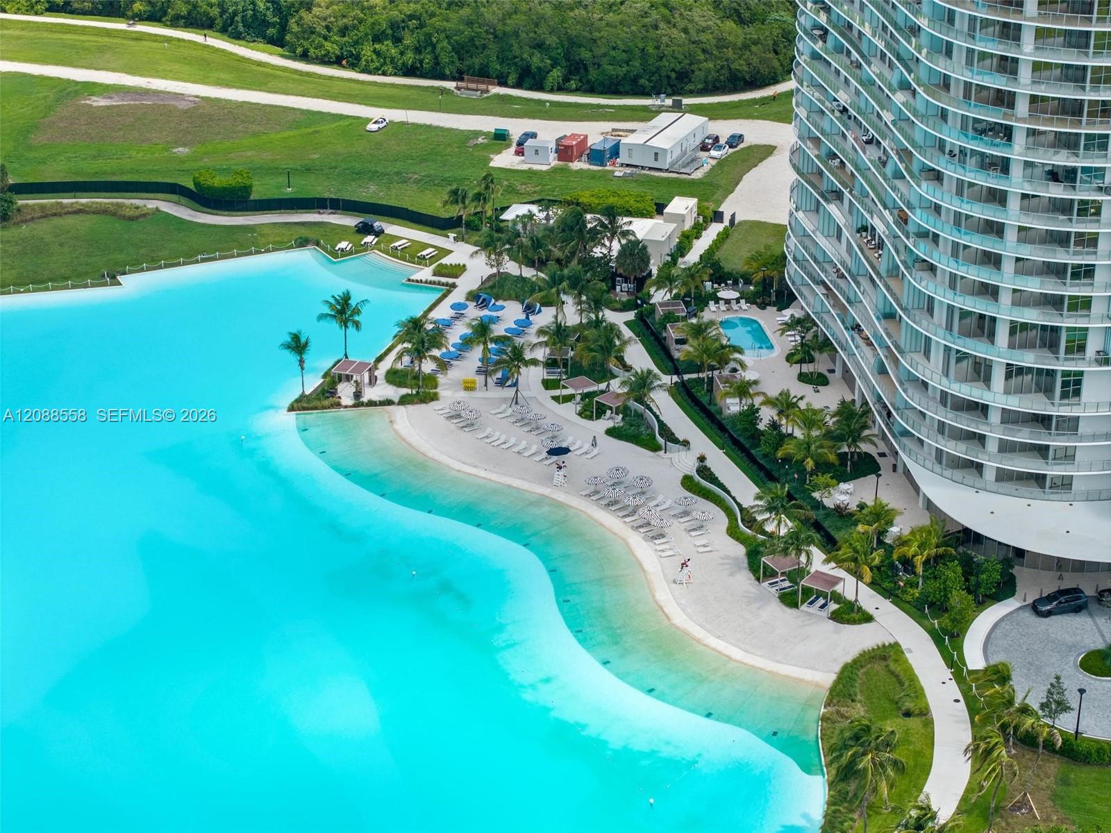 Aerial view of a condominium beside a turquoise lagoon-style pool and palm-lined lounging areas.
