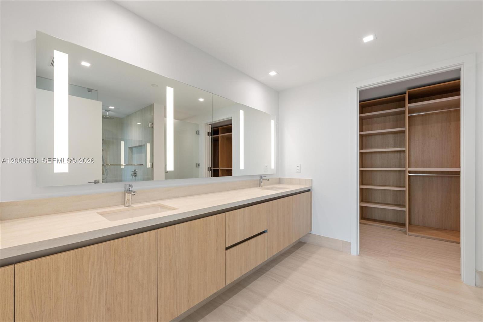 Bathroom with a long double vanity, wall-to-wall mirror, and open built-in closet.