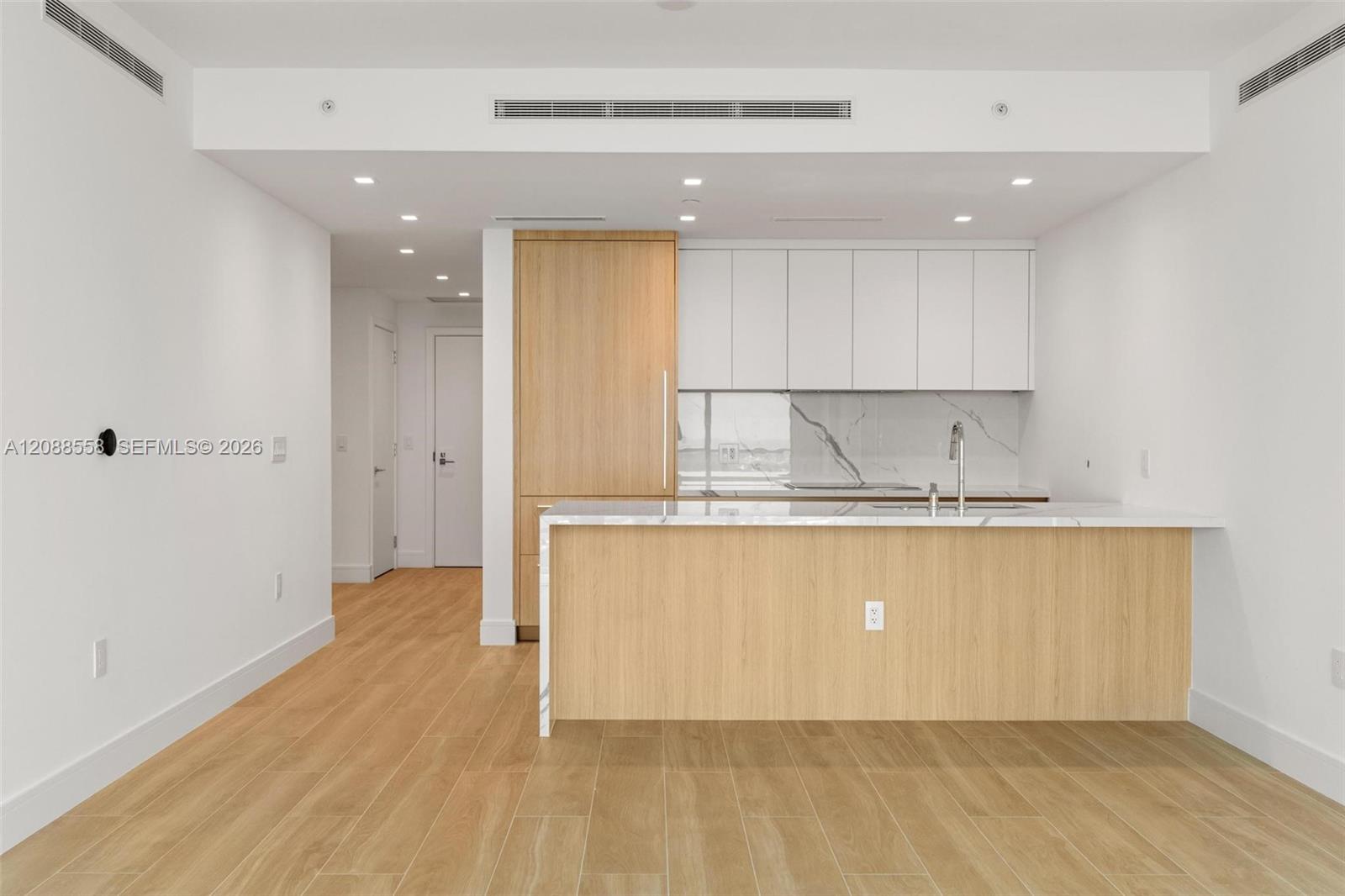 Unfurnished modern kitchen with light wood cabinetry, a wide peninsula, and marble-look backsplash.