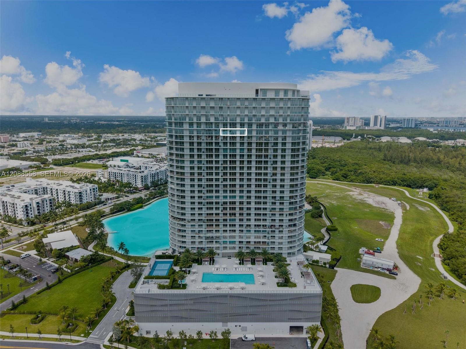 Aerial view of a curved residential tower, with one unit outlined above pools and landscaped grounds.