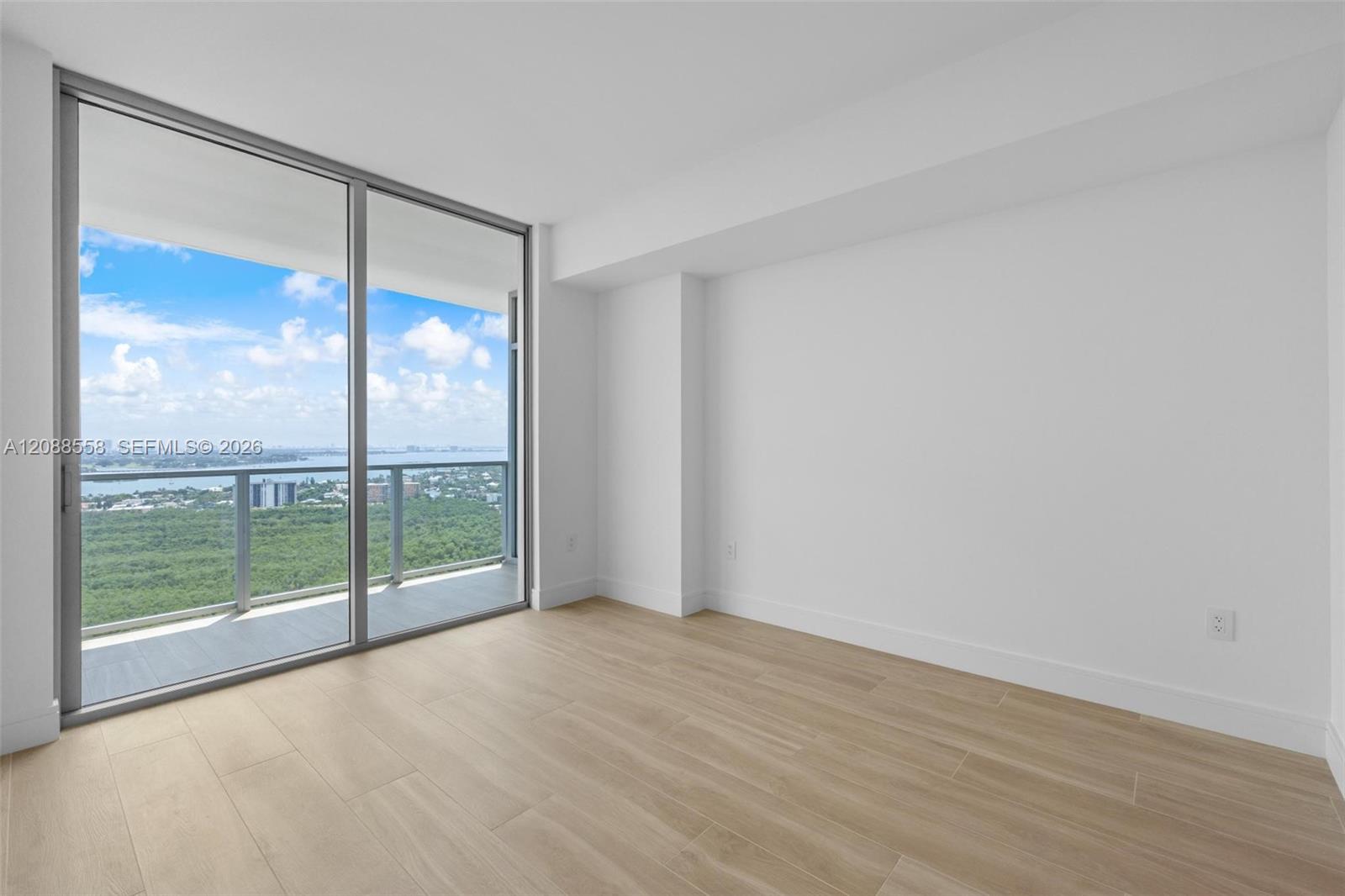 Vacant high-rise room with tile floors and sliding doors overlooking greenery, water, and distant buildings.