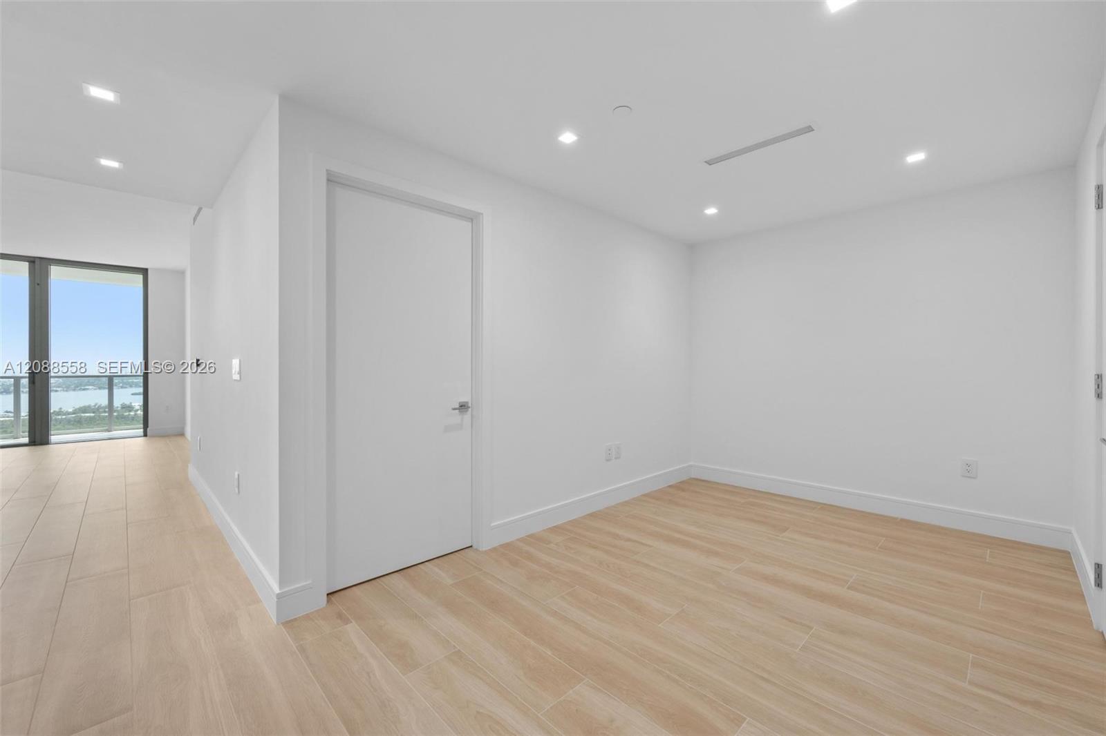 Empty room with light wood-look tile flooring and a view of water through the adjoining glass doors.