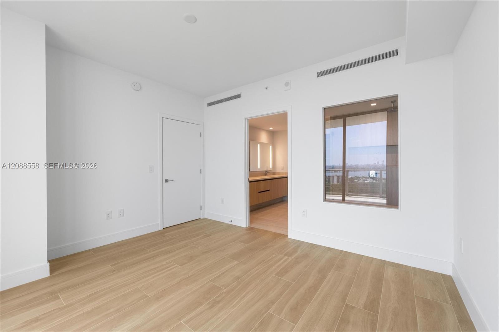 Vacant bedroom with wood-look tile floors and a window overlooking the water and city.