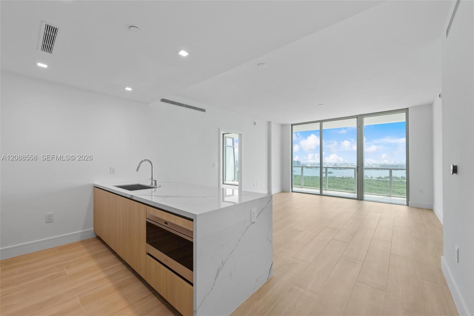 Vacant modern kitchen and living area with a waterfall island and balcony views of water and skyline.