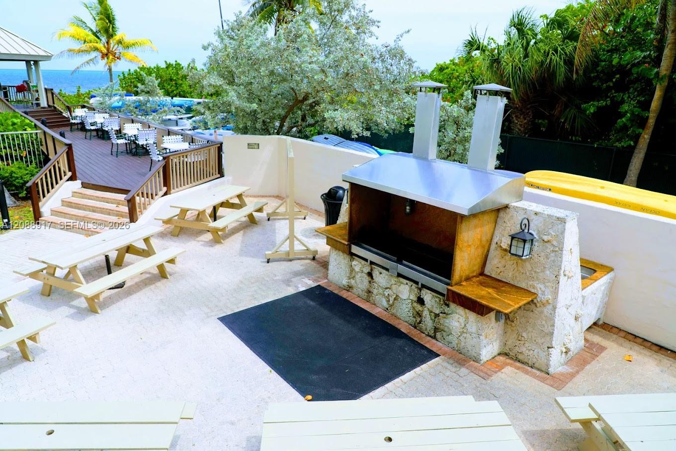 Outdoor patio with a stone barbecue, picnic tables, and a glimpse of the ocean.