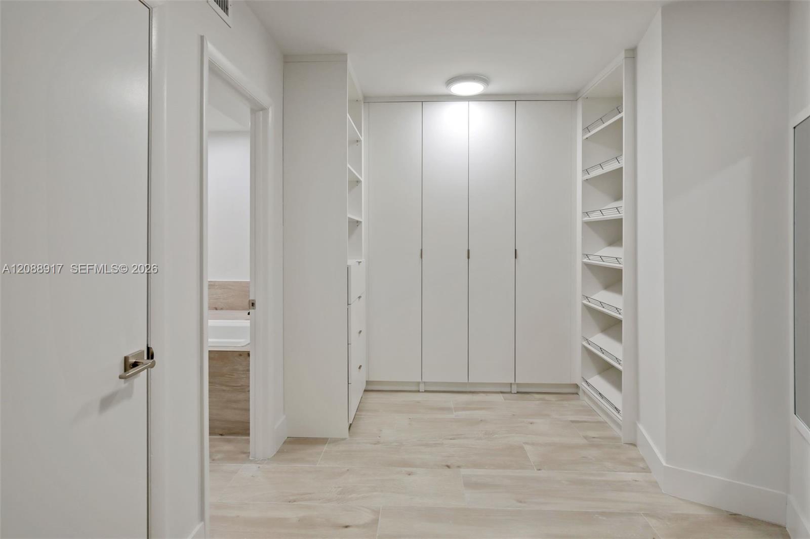 Walk-in closet with floor-to-ceiling white cabinets, built-in drawers, and open shelving.