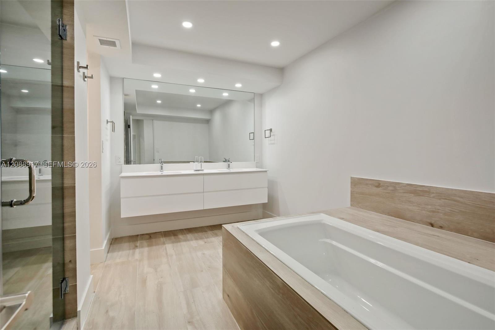 Modern bathroom with a large built-in tub, floating double vanity, and glass-enclosed shower.