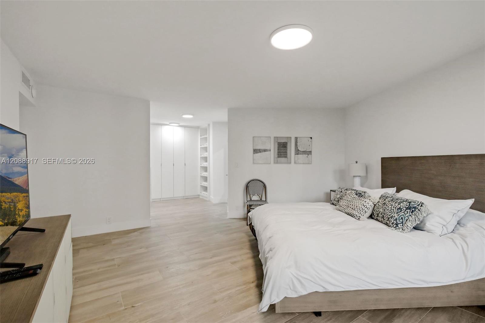 Bedroom with a large bed, wood headboard, patterned pillows, and built-in white closets.