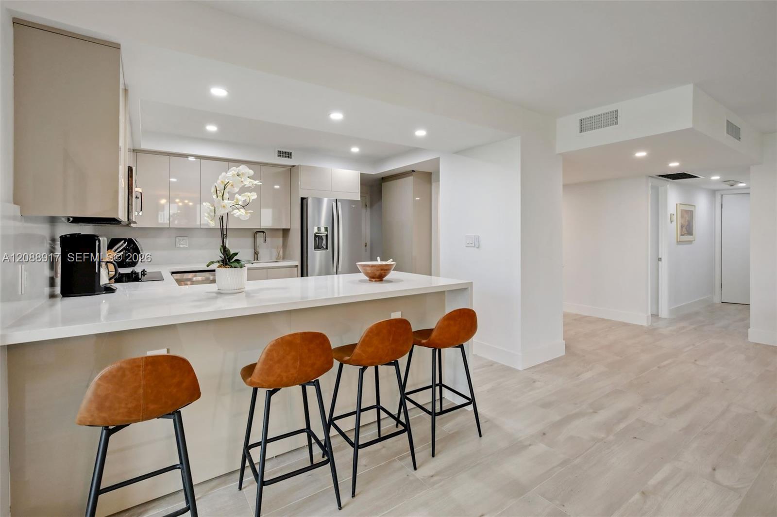 Modern condo kitchen with glossy pale cabinets, stainless refrigerator, and rust-colored stools at a white island.