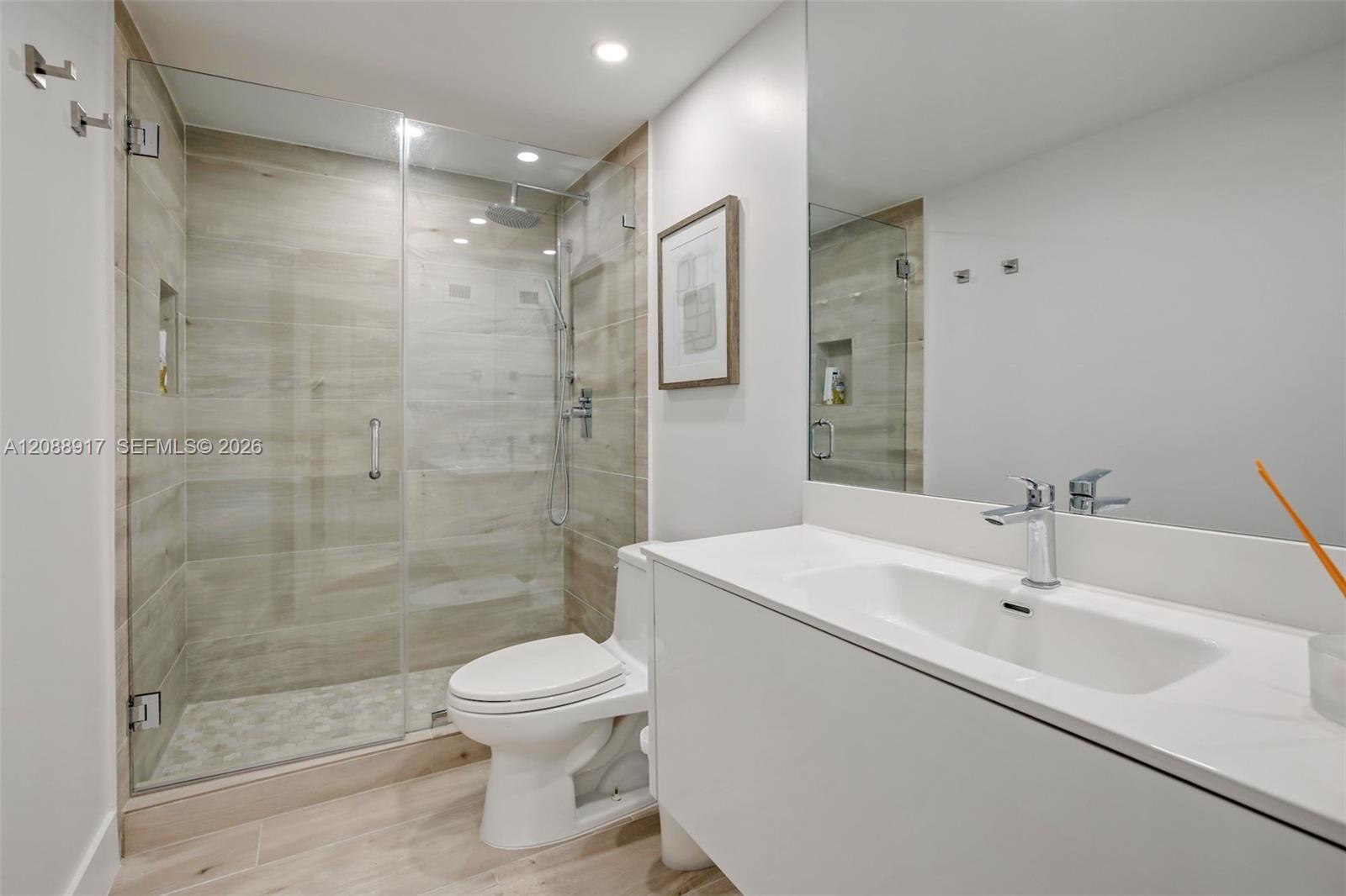 Modern bathroom with a glass walk-in shower, beige tile, and long white vanity.