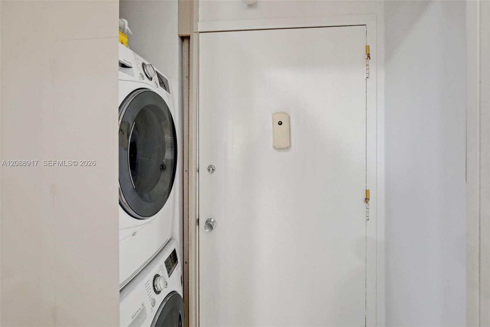 Stacked washer and dryer in a narrow laundry closet beside a white door.
