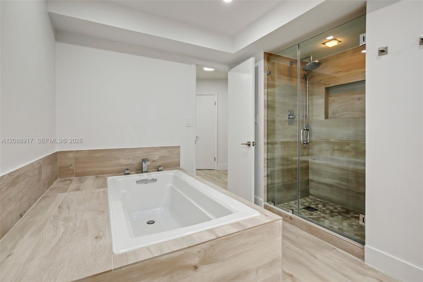 Bathroom with a built-in soaking tub and glass-enclosed tiled shower.