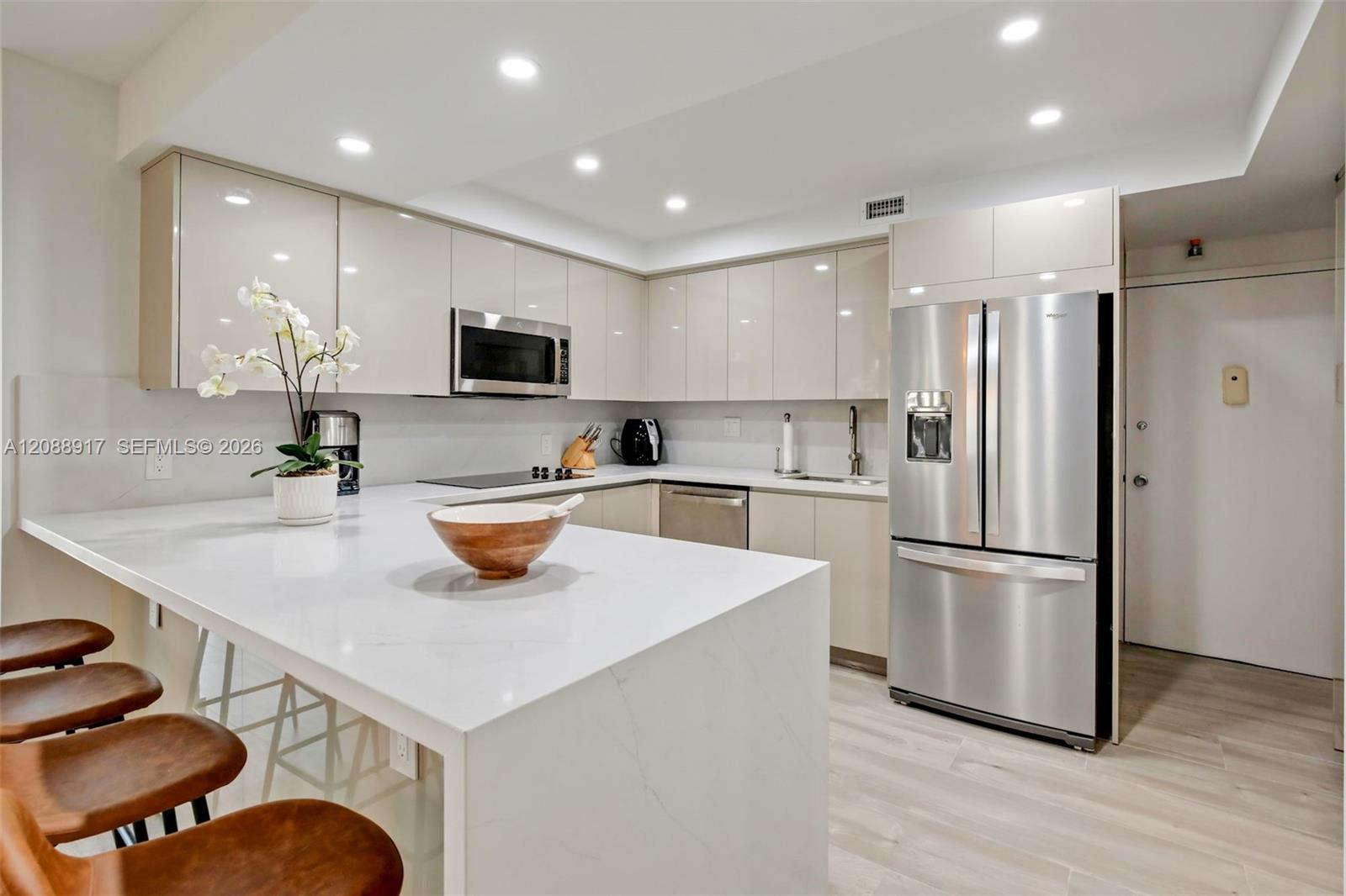 Modern condo kitchen with a large white island, glossy cabinets, and stainless steel refrigerator.