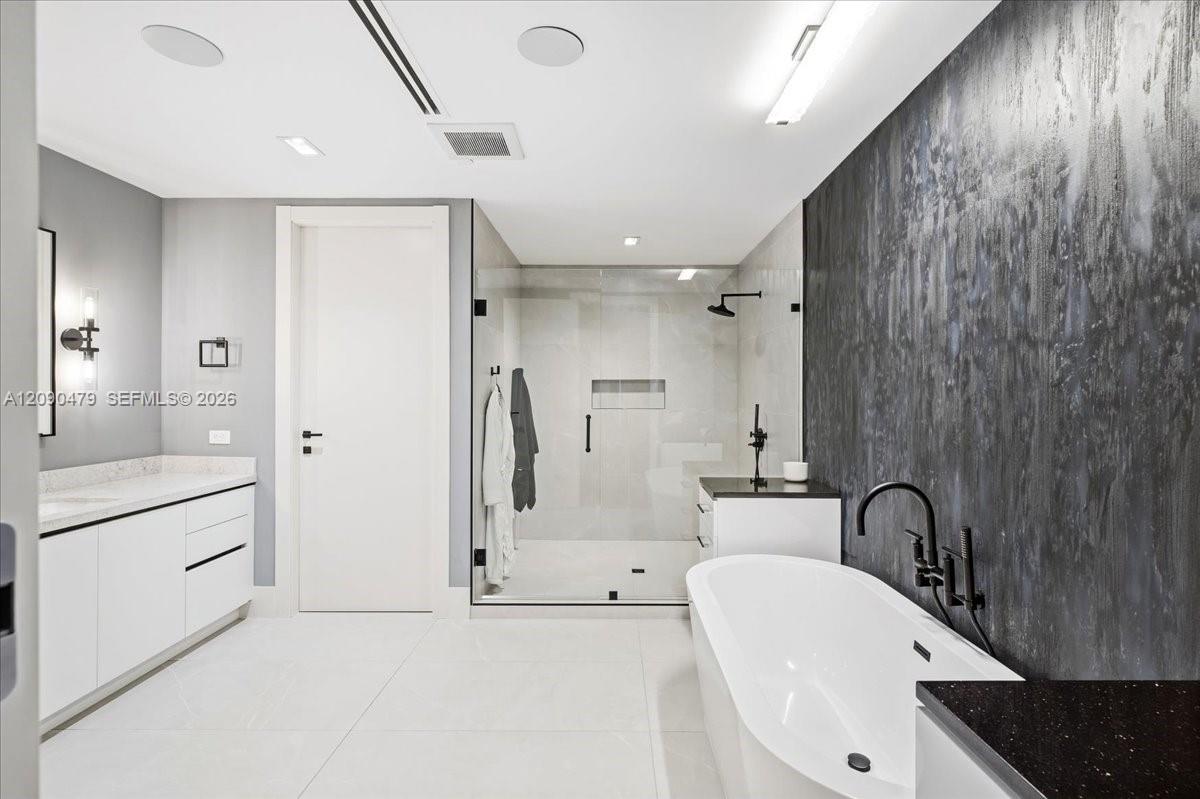 Modern bathroom with a freestanding tub, dark accent wall, glass shower, and white vanity.