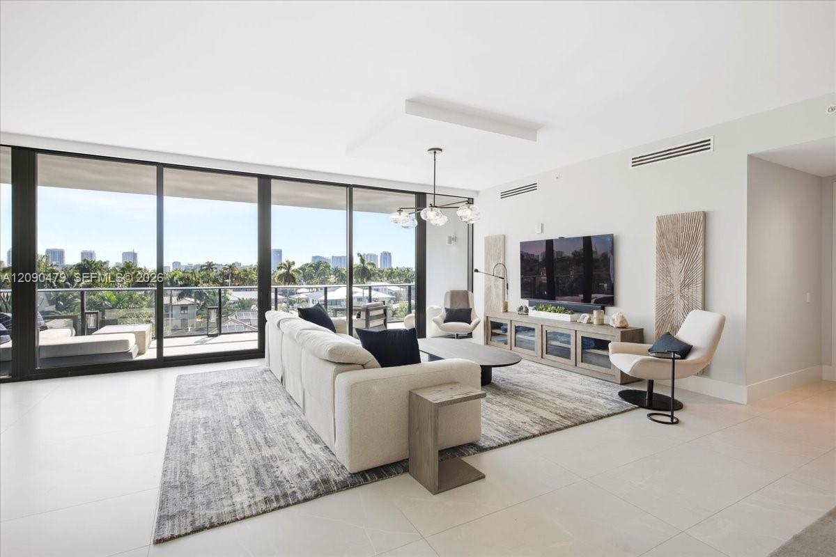 Furnished living room with a white sectional and floor-to-ceiling windows overlooking palms and distant buildings.