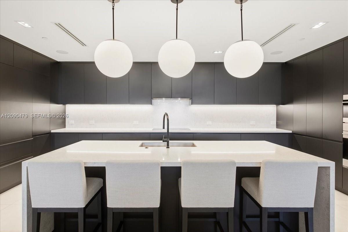 Modern kitchen with a white waterfall island, dark cabinetry, and three spherical pendant lights.