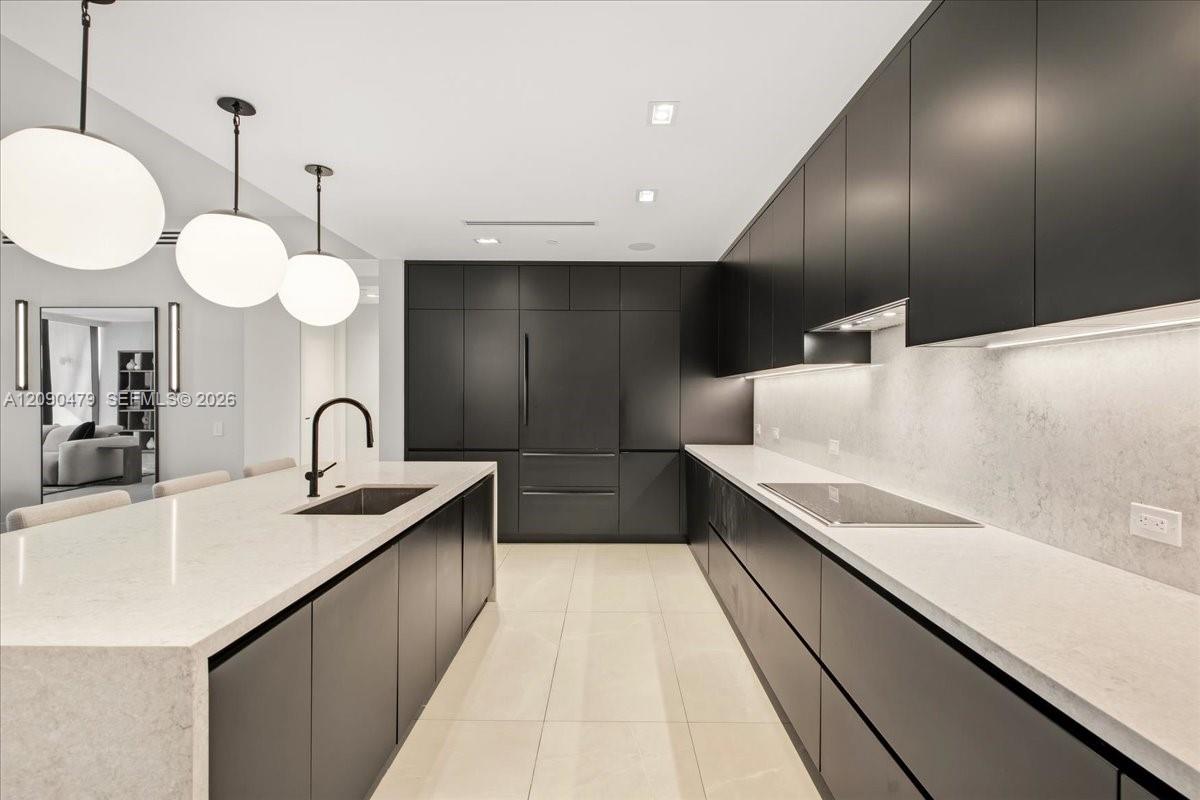 Modern kitchen with dark cabinetry, white stone counters, a large island, and globe pendant lights.