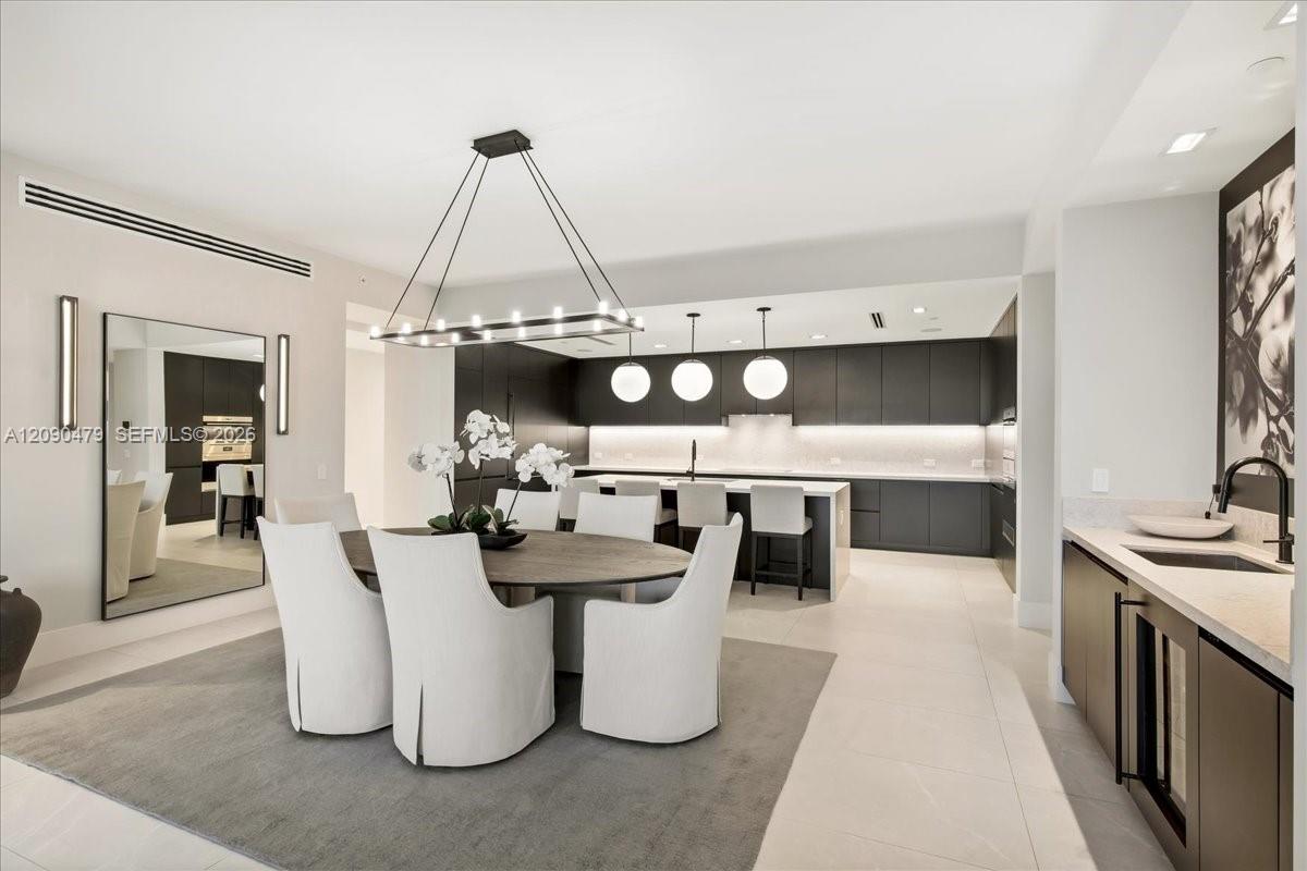 Open-plan dining room and kitchen with a round table, white chairs, and dark cabinetry.