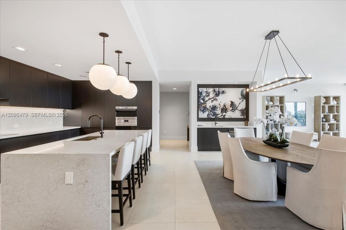 Open-concept kitchen and dining area with a large stone island, dark cabinetry, and sculptural pendant lights.