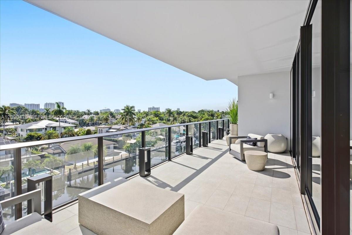 Condominium balcony with modern seating overlooking a canal and palm-lined neighborhood.