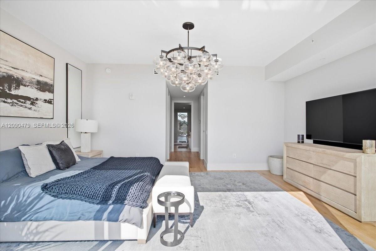 Furnished bedroom with a blue bed, glass-bubble chandelier, and light wood dresser.