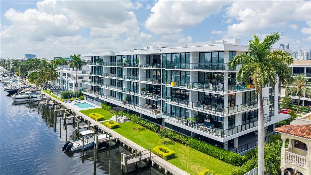 Modern waterfront condominium with glass balconies, marina docks, boats, and a pool.
