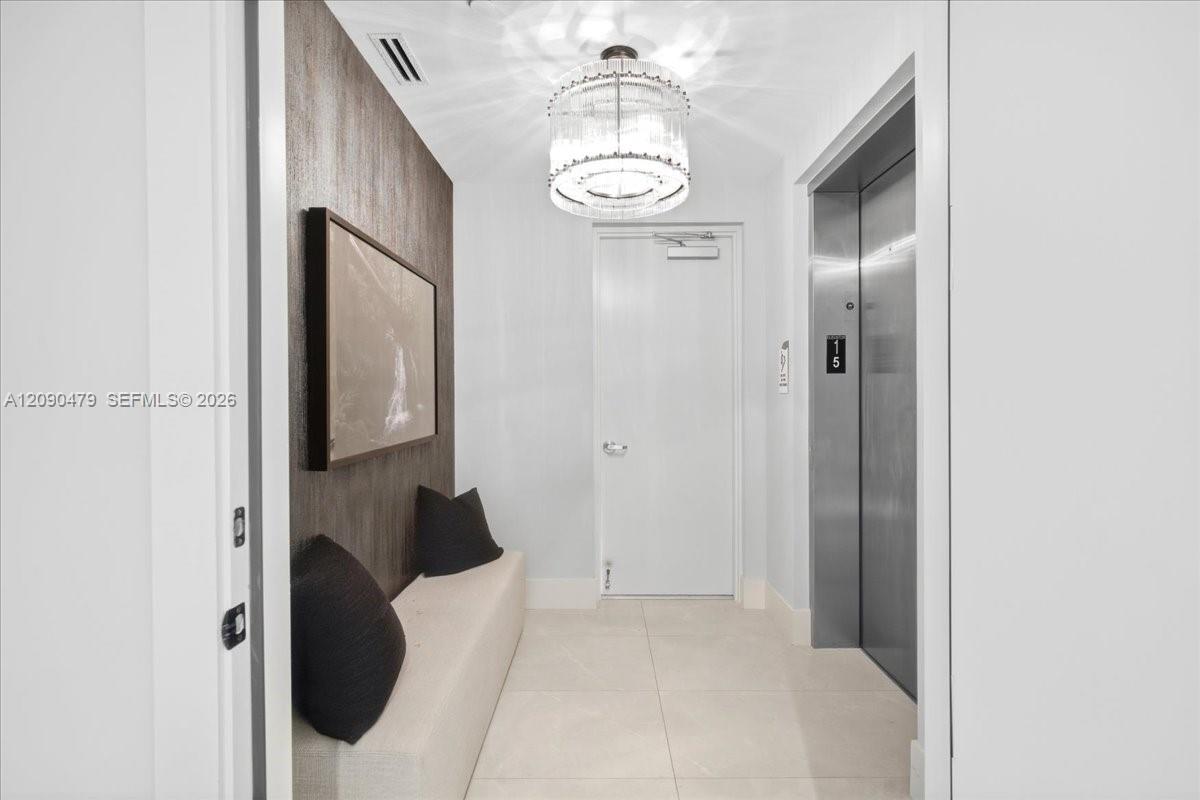 Condo entry hall with a cream bench, framed artwork, chandelier, and stainless-steel elevator.