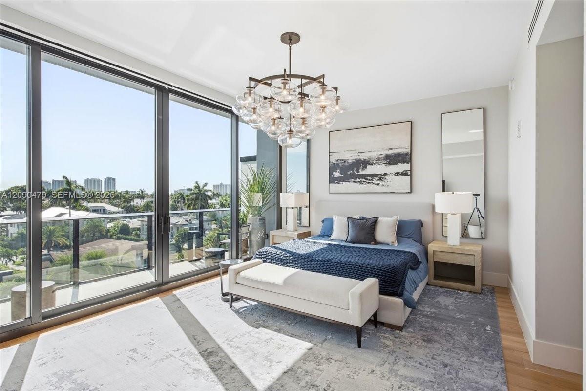 Primary bedroom with a blue bed, glass chandelier, and floor-to-ceiling windows overlooking a palm-lined neighborhood.
