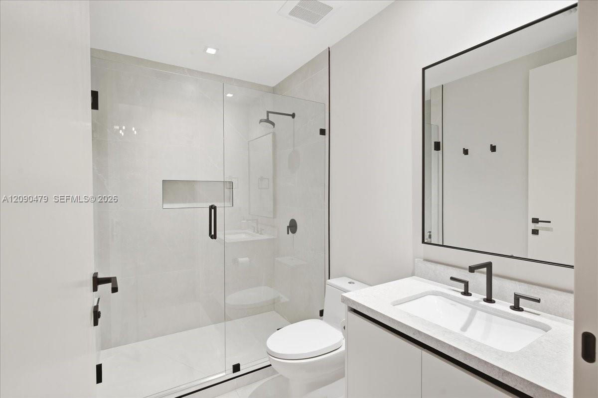 Modern bathroom with glass shower, recessed niche, wall-mounted toilet, and white vanity with black fixtures.