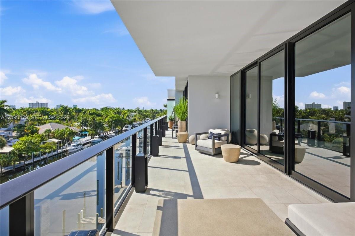 Condo terrace with glass railings and lounge chairs overlooking a tree-lined waterway.
