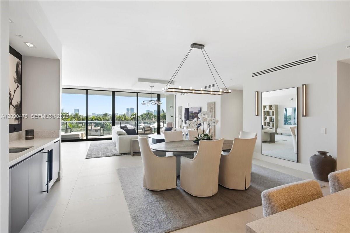 Open-plan dining and living area with a round table, modern kitchen, and floor-to-ceiling windows overlooking palm trees.
