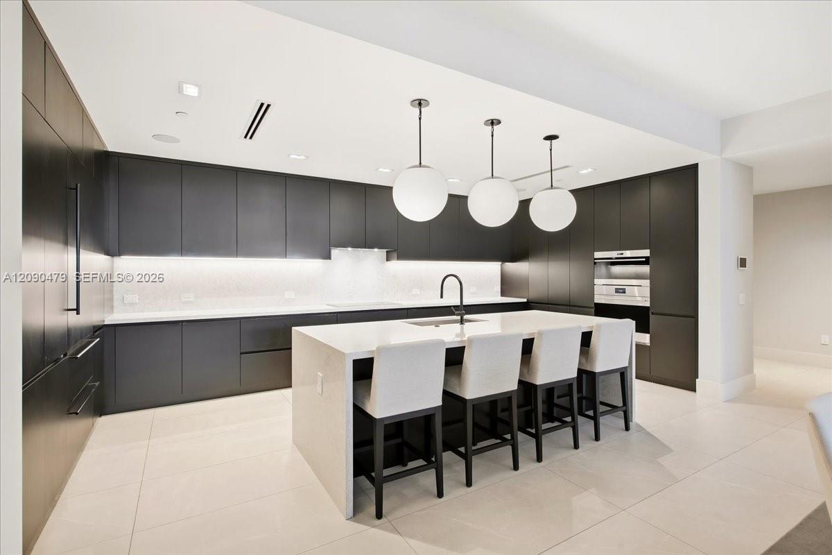 Modern kitchen with dark cabinets, a white island, four bar stools, and globe pendant lights.
